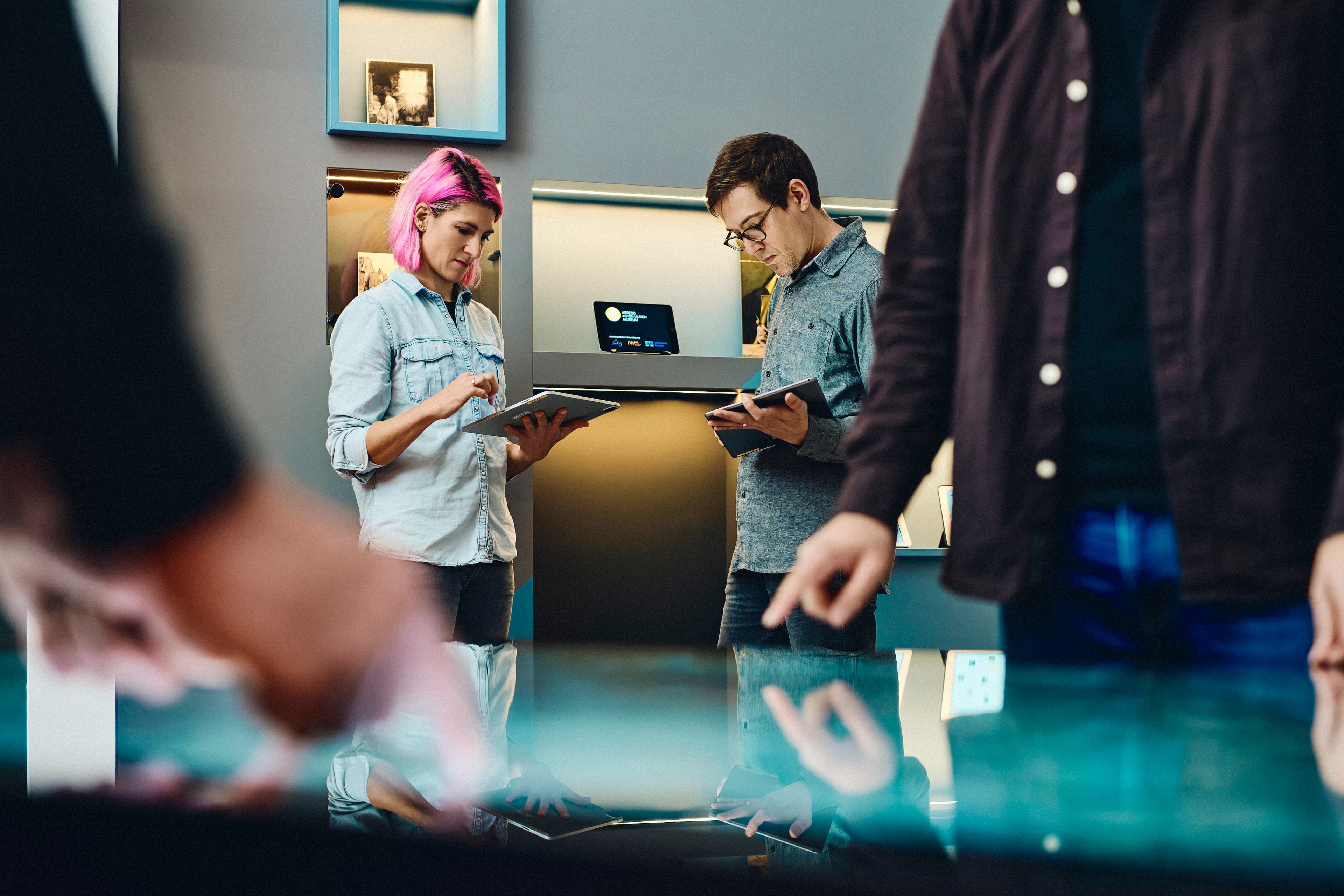 Zwei Personen bedienen einen Multi-Touch-Tisch und im Hintergrund stehen zwei Personen mit Tablets